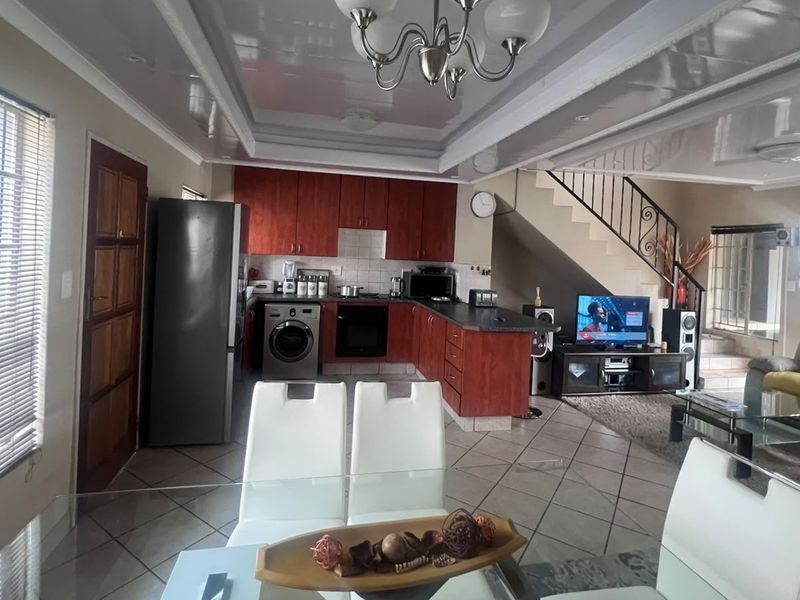 Open-plan living and kitchen area featuring tiled flooring, built-in cabinetry, and a staircase with metal railing, offering a functional layout for modern living.
