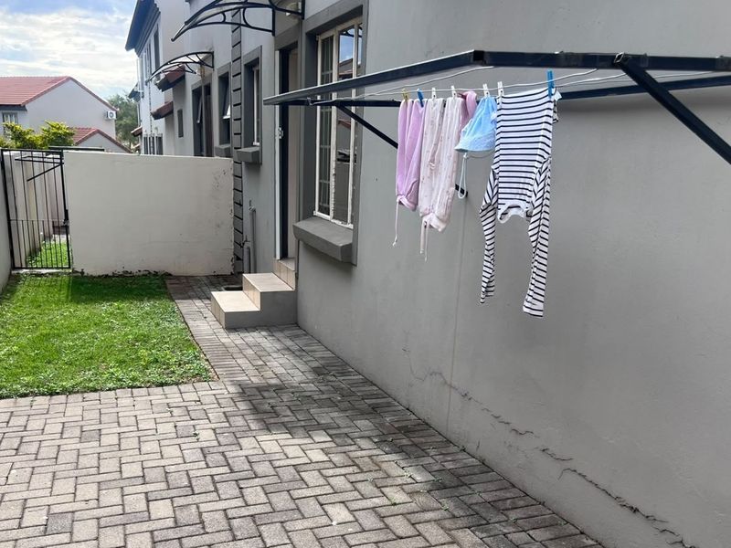 A rear courtyard area featuring paved flooring, a small lawn, boundary walls, and a wall-mounted clothesline attached to the townhouse exterior.