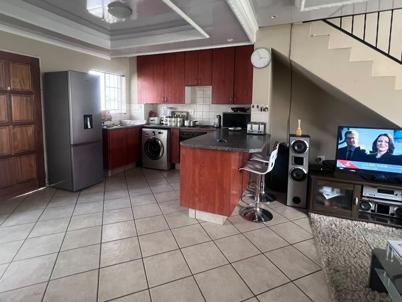 Open-plan living and kitchen area featuring tiled flooring, wooden cabinetry, and a staircase with a metal railing.