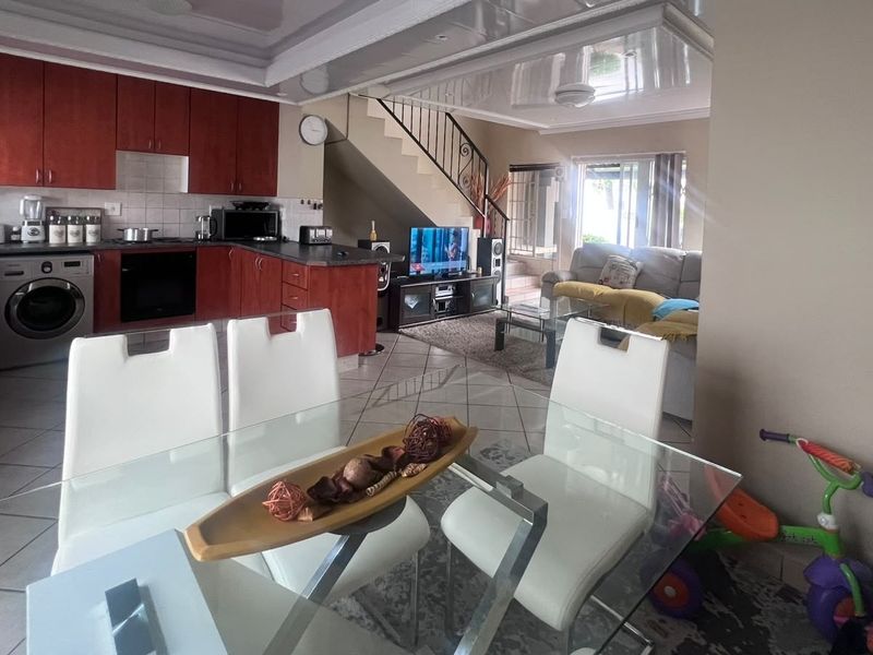 Open-plan living area featuring a kitchen with built-in cabinetry, integrated appliances, and tiled flooring, seamlessly flowing into the dining and lounge space.