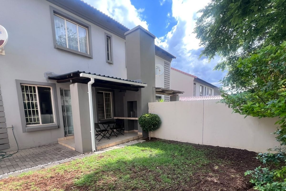 Rear exterior view of the townhouse featuring a covered patio with a built-in braai, paved flooring, and a private garden area.