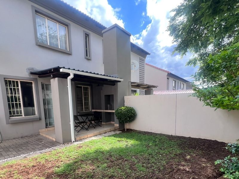 Rear exterior view of the townhouse featuring a covered patio with a built-in braai, paved flooring, and a private garden area.