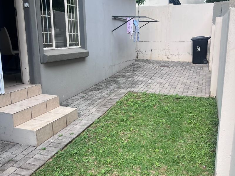 A rear courtyard area featuring a paved section, small lawn, and wall-mounted drying rack, providing a functional outdoor space for the townhouse.