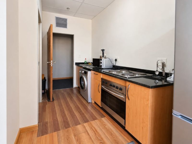 Compact kitchen featuring built-in oven, electric hob, granite countertops, and wood-look laminate flooring with direct access to an adjacent room.