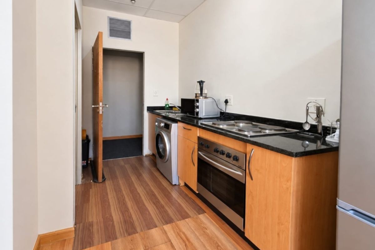 Compact kitchen featuring built-in oven, electric hob, granite countertops, and wood-look laminate flooring with direct access to an adjacent room.