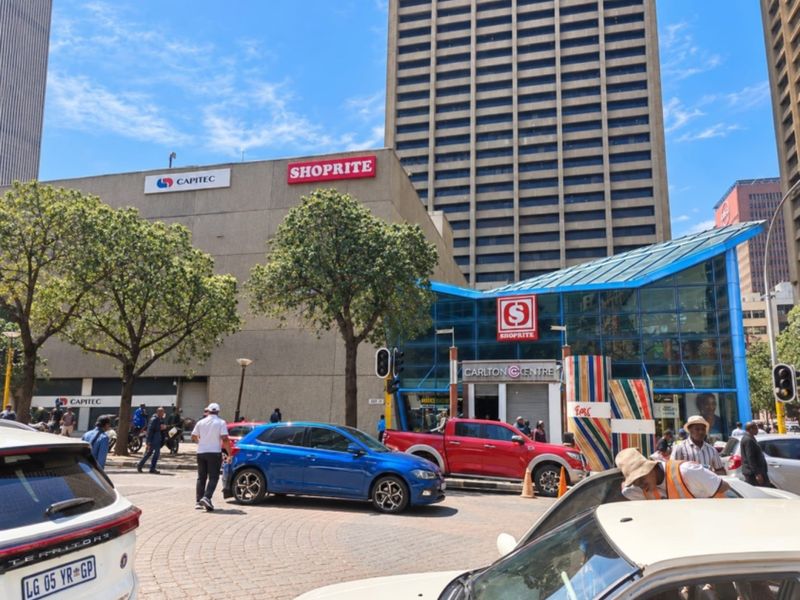 Street level view of the Carlton Centre commercial building entrance featuring a glass atrium and surrounding urban infrastructure.