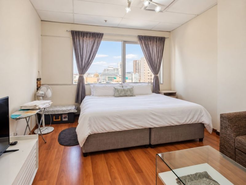 A bedroom featuring laminate flooring, a drop ceiling, and a large window offering expansive city views.