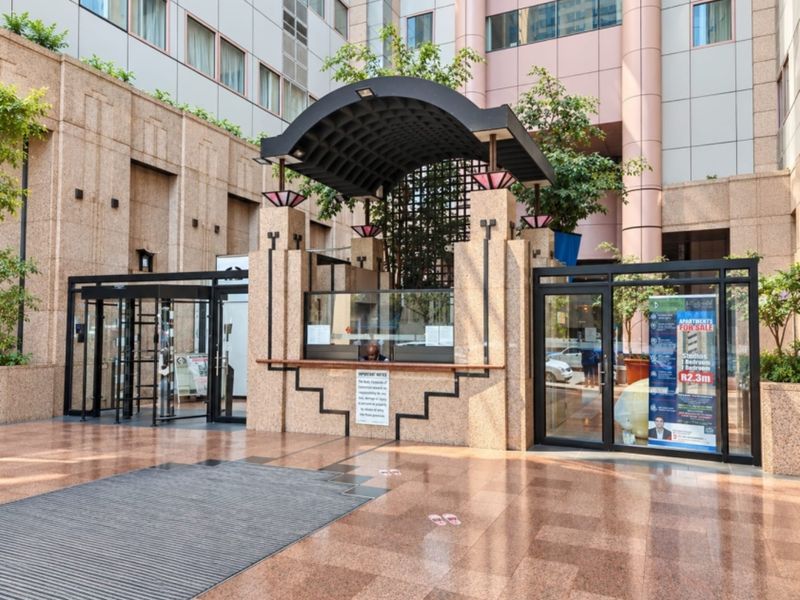 Main entrance area of the apartment complex featuring a secure guard booth, revolving doors, and polished granite flooring.