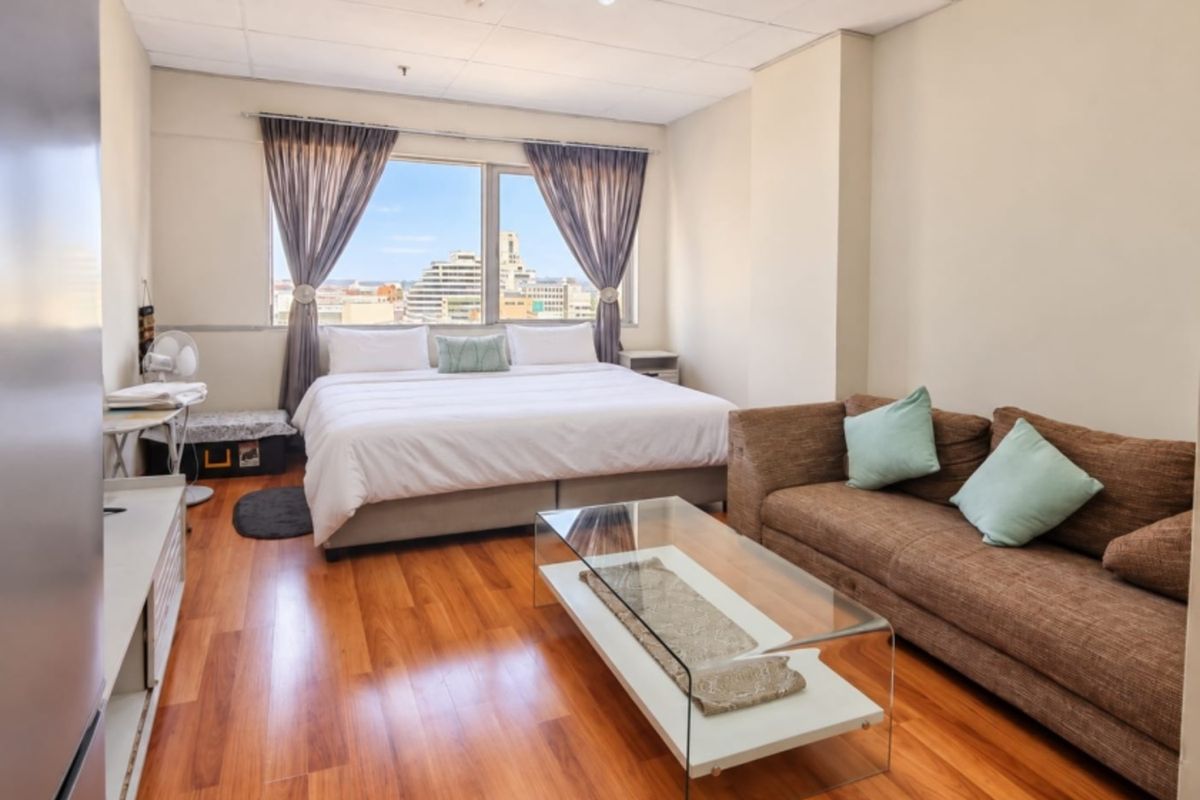 A spacious bedroom featuring laminate flooring, a drop ceiling, and a large window offering city views.