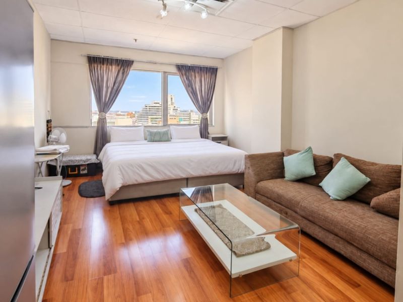 A spacious bedroom featuring laminate flooring, a drop ceiling, and a large window offering city views.