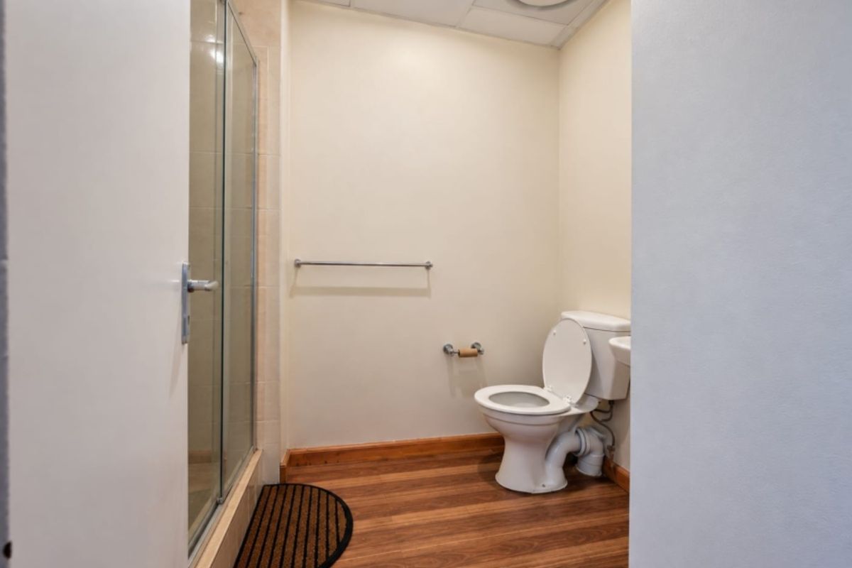 A functional bathroom featuring a shower enclosure, toilet, and laminate flooring, with a drop ceiling and neutral wall finishes.