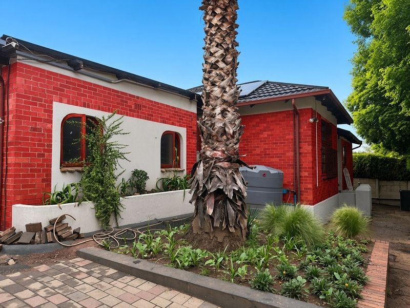 Rear exterior view of the house featuring a red brick facade, arched windows, a paved patio area, and a water storage tank.