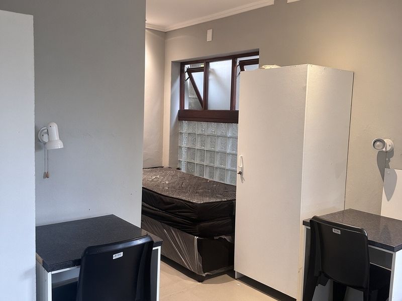 A functional bedroom space featuring neutral grey walls, recessed lighting, and a unique glass block window detail.