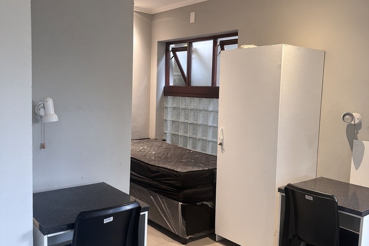 A functional bedroom space featuring neutral grey walls, recessed lighting, and a unique glass block window detail.