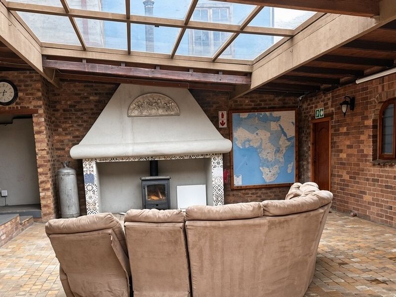 A covered patio area featuring exposed brick walls, a large glass skylight, and a built-in fireplace with a wood-burning stove.