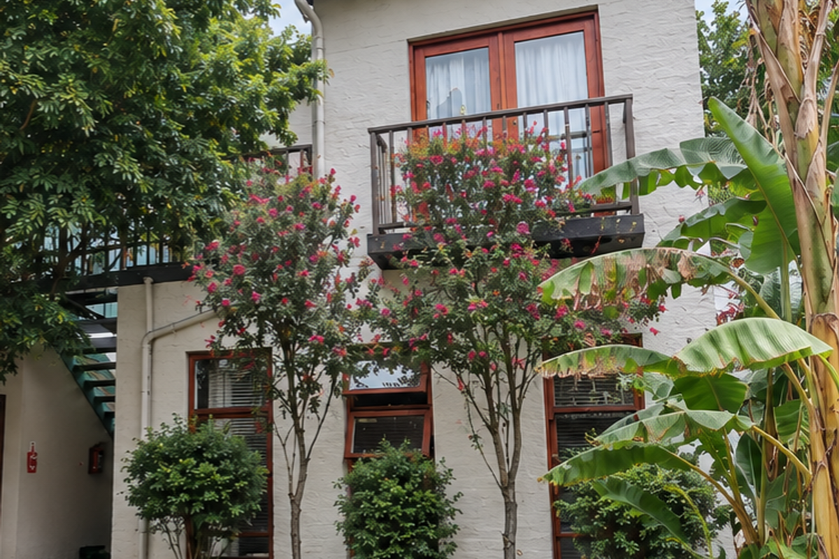 A two-story residential facade featuring timber-framed windows and doors, a balcony with metal railings, and an external staircase set within a landscaped garden.