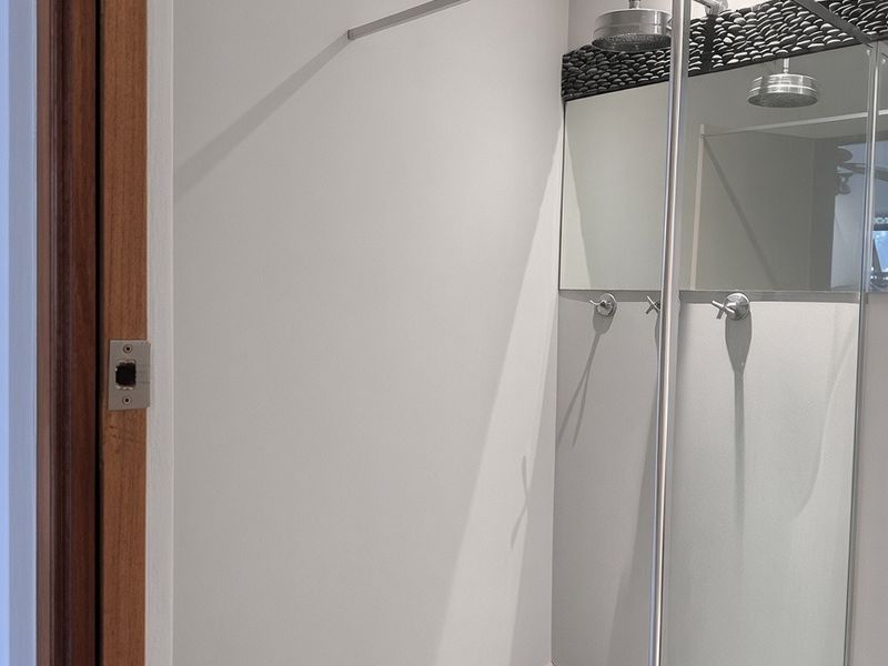 Modern walk-in shower featuring a rain shower head, glass enclosure, and distinctive black pebble tile flooring with recessed lighting.