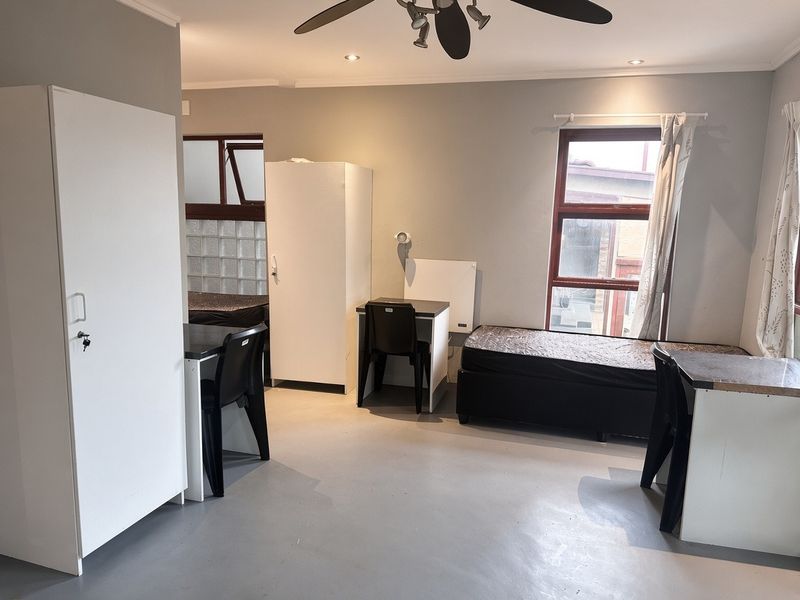 A functional bedroom featuring a ceiling fan, recessed lighting, and glass block accents, providing a neutral space with practical window placement.