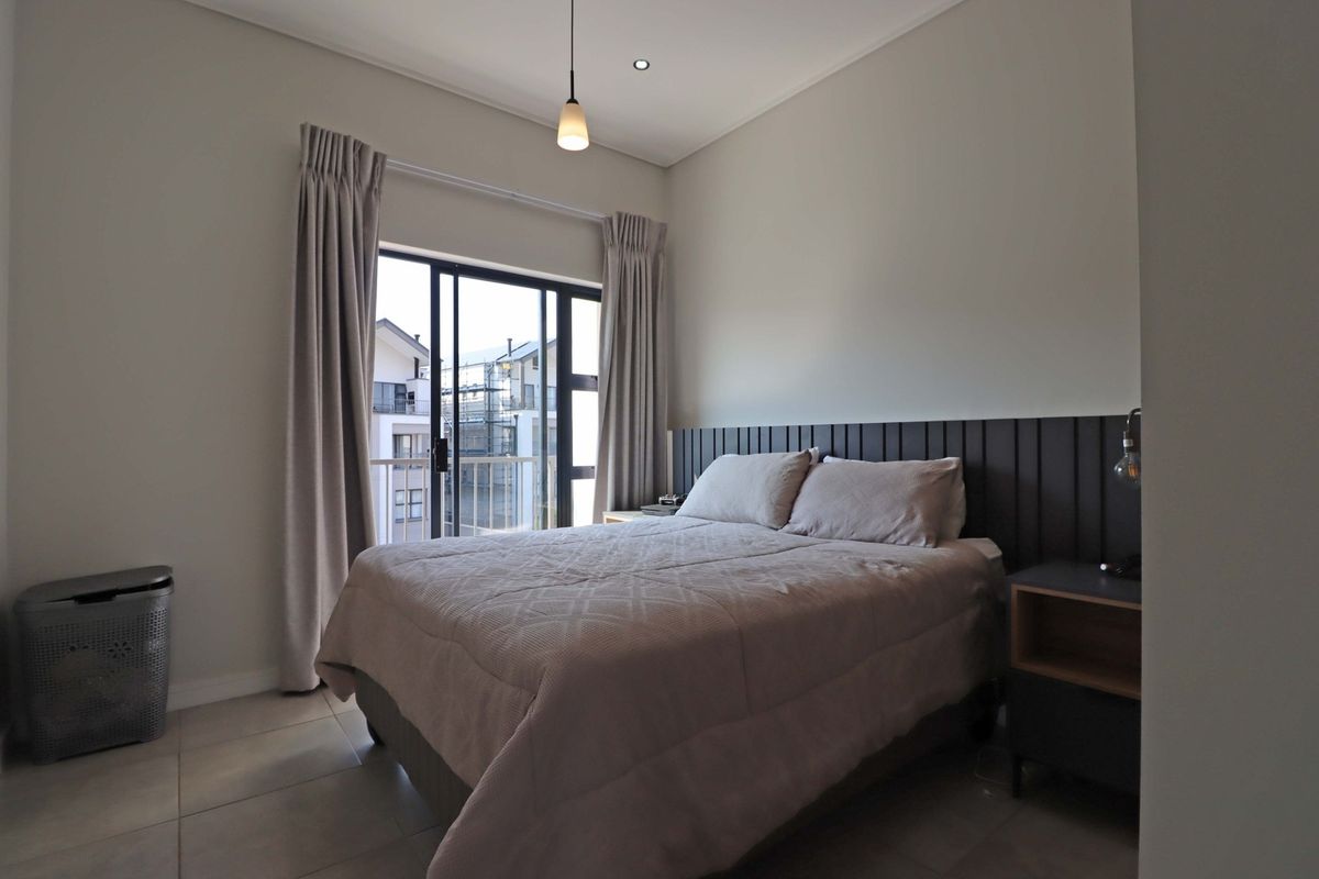 A well-maintained bedroom featuring tiled flooring, a modern built-in headboard, and a sliding glass door providing access to a balcony.