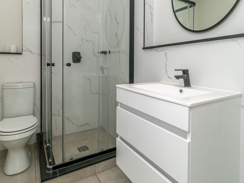Modern bathroom featuring a glass shower enclosure, white vanity with basin, and marble-look wall tiles with contemporary black fixtures.