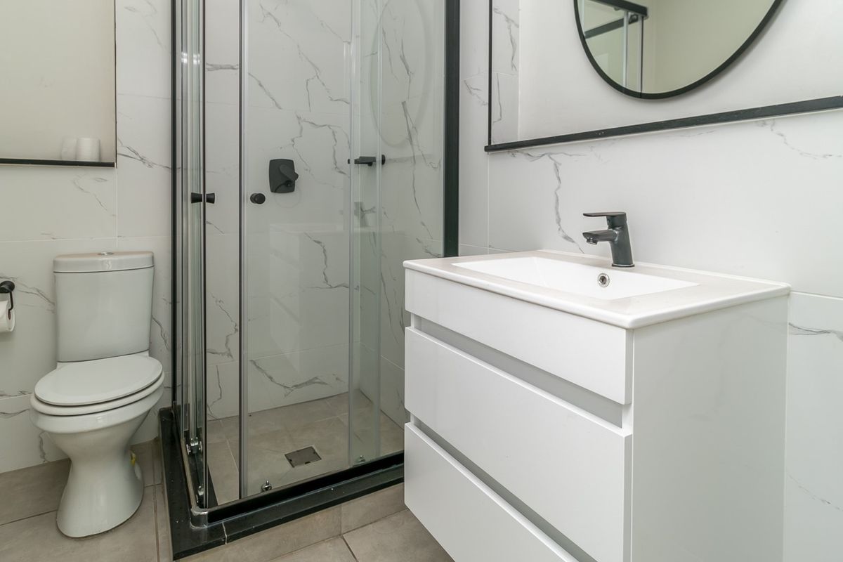 Modern bathroom featuring a glass shower enclosure, white vanity with basin, and marble-look wall tiles with contemporary black fixtures.