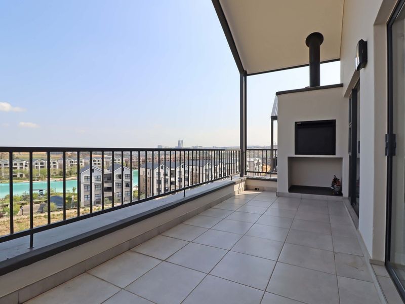 Spacious covered balcony featuring a built-in braai, tiled flooring, and a metal balustrade with expansive views of the surrounding estate.