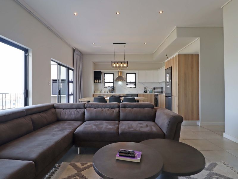 Modern open-plan living area featuring a contemporary kitchen with sleek cabinetry, stone countertops, and seamless flow to the balcony through large sliding glass doors.