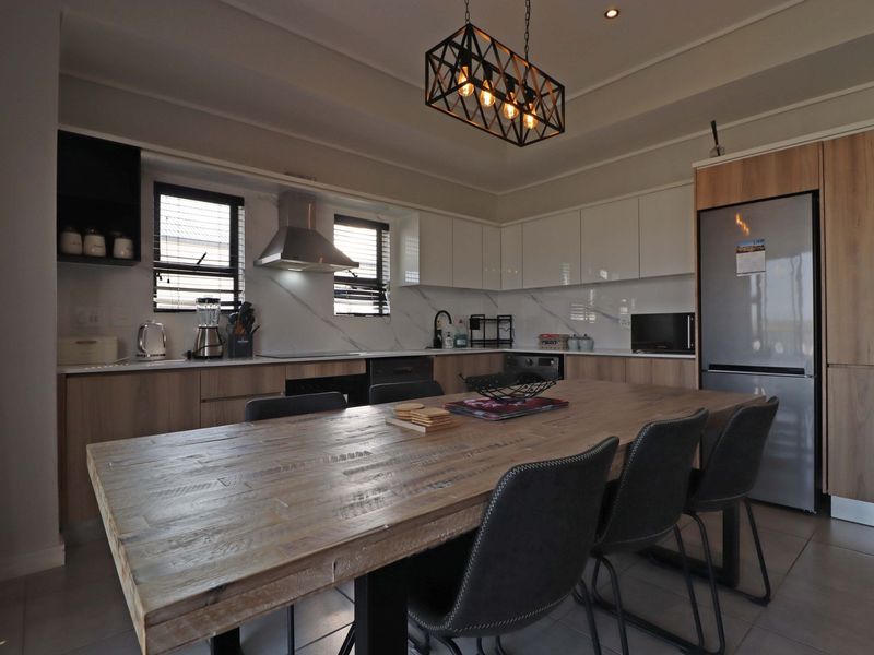Modern open-plan kitchen and dining area featuring sleek cabinetry, stone-look backsplash, integrated appliances, and contemporary pendant lighting.