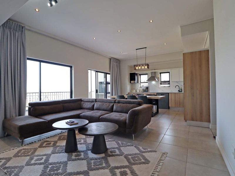 Modern open-plan living area featuring tiled floors, recessed lighting, and a contemporary kitchen with integrated cabinetry and island, flowing onto a balcony.