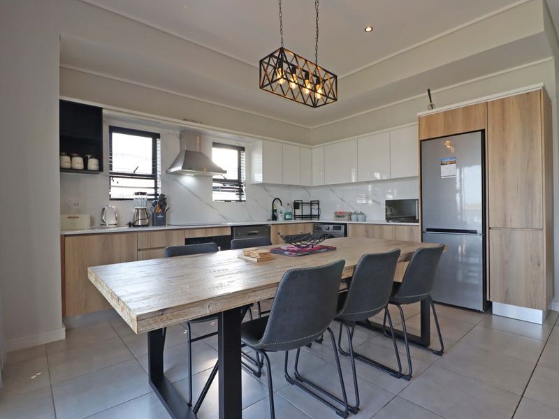 Modern open-plan kitchen and dining area featuring sleek cabinetry, marble-look splashback, integrated appliances, and contemporary pendant lighting.