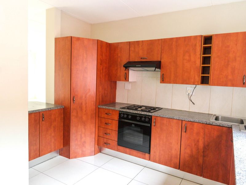 A functional kitchen featuring wood-look laminate cabinetry, granite countertops, built-in oven with hob, extractor fan, and tiled flooring.