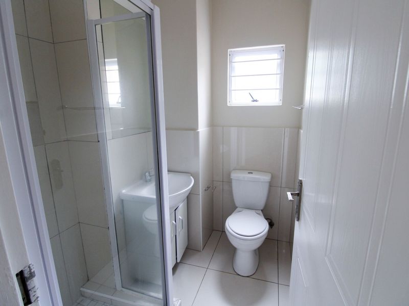 A clean and functional bathroom featuring a shower enclosure, vanity basin, and toilet with neutral tiled finishes throughout.