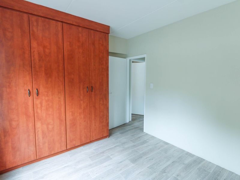 A clean, empty bedroom featuring modern laminate flooring and a large, built-in wooden wardrobe.