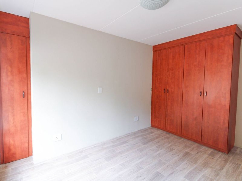 A bright, empty bedroom featuring modern laminate flooring and extensive built-in wooden cupboards, offering ample storage space.