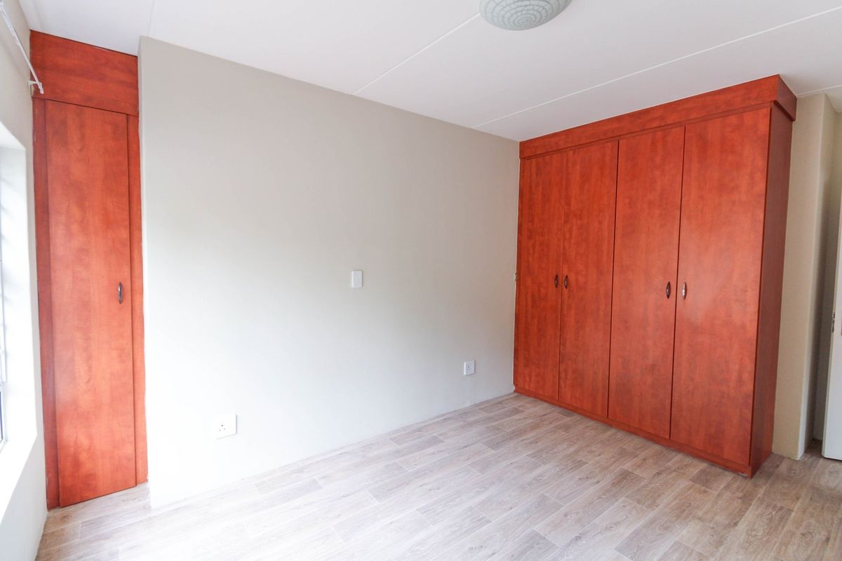 A bright, empty bedroom featuring modern laminate flooring and extensive built-in wooden cupboards, offering ample storage space.