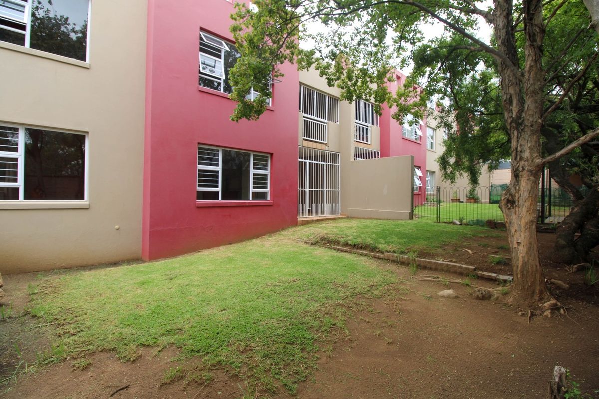 Rear view of the apartment building featuring a private garden area with security bars on windows and doors.