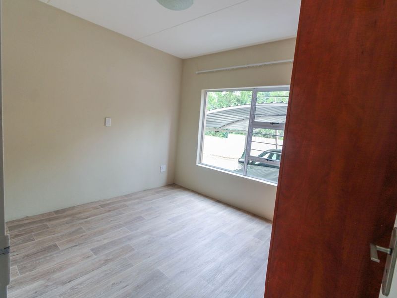 A bright, empty bedroom featuring modern laminate flooring and a large window with an aluminium frame, offering a clean and neutral living space.