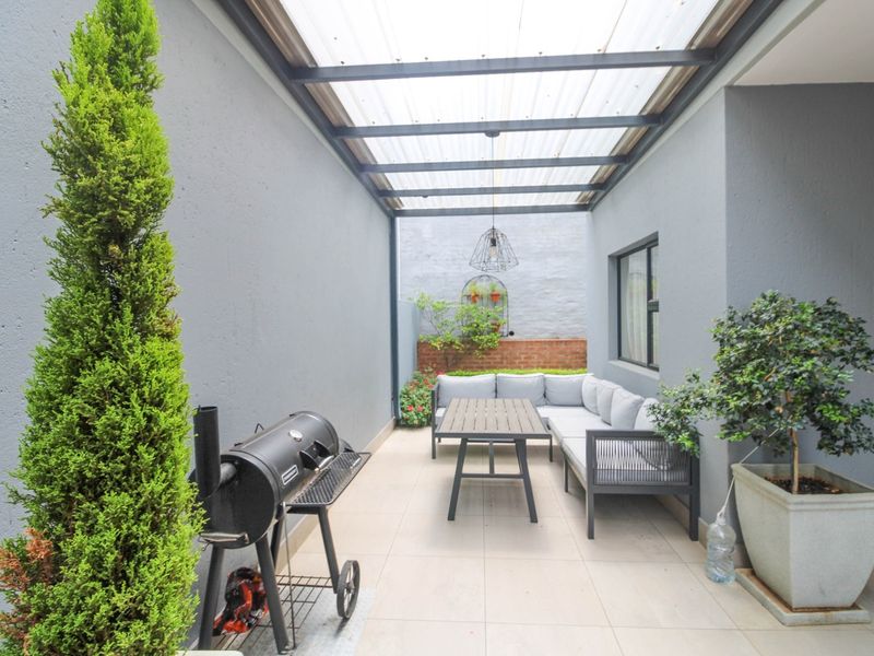 A covered outdoor patio area featuring tiled flooring, a translucent roof structure, and a pendant light, providing a functional space for outdoor living.