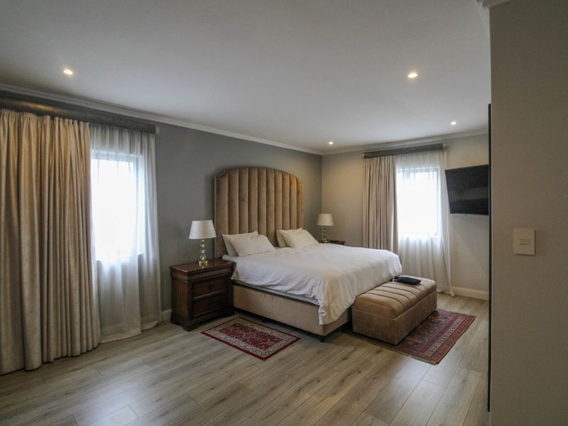 Spacious bedroom featuring modern laminate flooring, recessed downlighting, and dual windows with fitted curtain tracks.