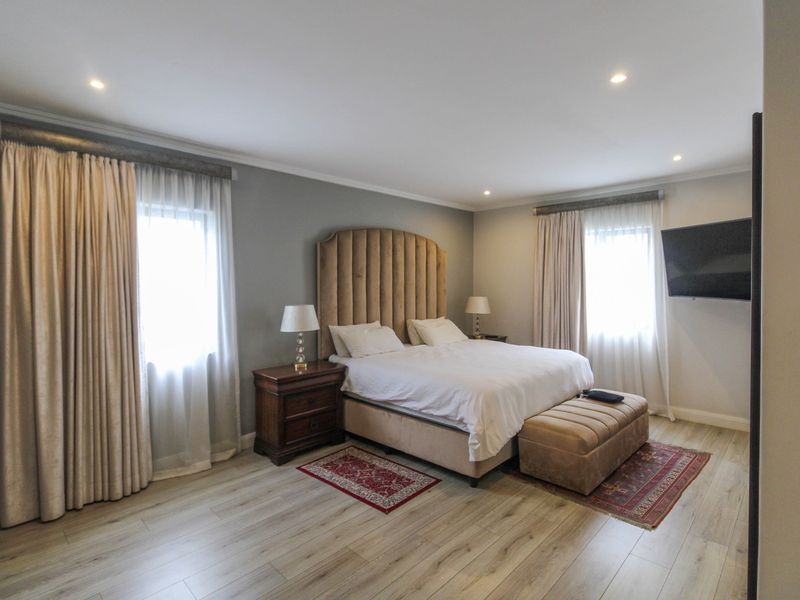 Spacious bedroom featuring light-toned laminate flooring, recessed downlighting, and dual windows with floor-to-ceiling curtains.