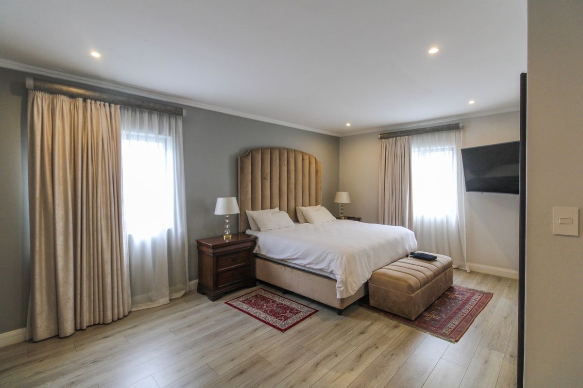 Spacious bedroom featuring light-toned laminate flooring, recessed downlighting, and dual windows with floor-to-ceiling curtains.