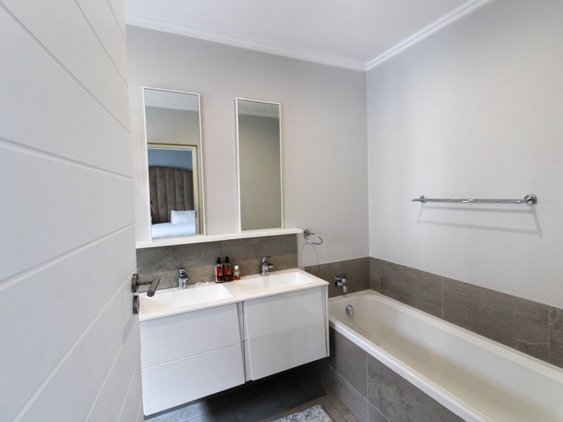 Modern bathroom featuring a double vanity with integrated sinks, wall-mounted mirrors, and a tiled bathtub surround.