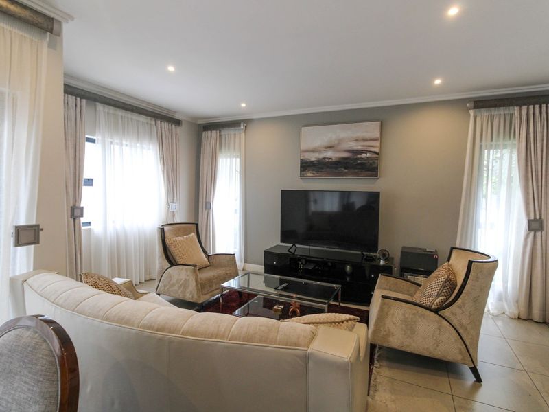 A well-maintained living room featuring tiled flooring, recessed downlighting, and large windows with fitted curtain tracks.