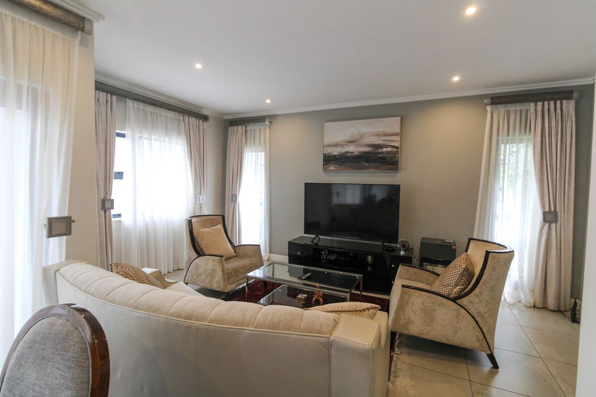 A well-maintained living room featuring tiled flooring, recessed downlighting, and large windows with fitted curtain tracks.