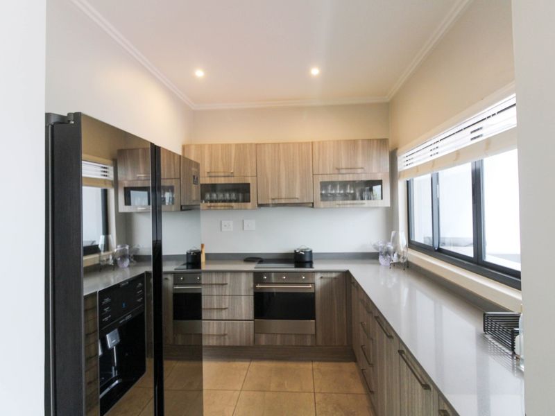 Modern kitchen featuring wood-grain cabinetry, stone countertops, integrated appliances, and ample natural light from the side window.