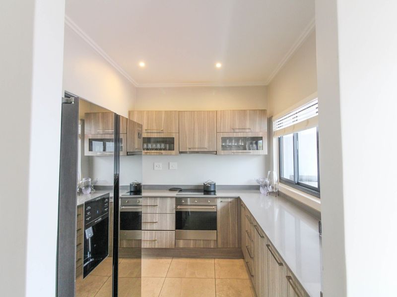 Modern kitchen featuring wood-finish cabinetry, stone countertops, integrated appliances, and tiled flooring, offering a clean and functional workspace.