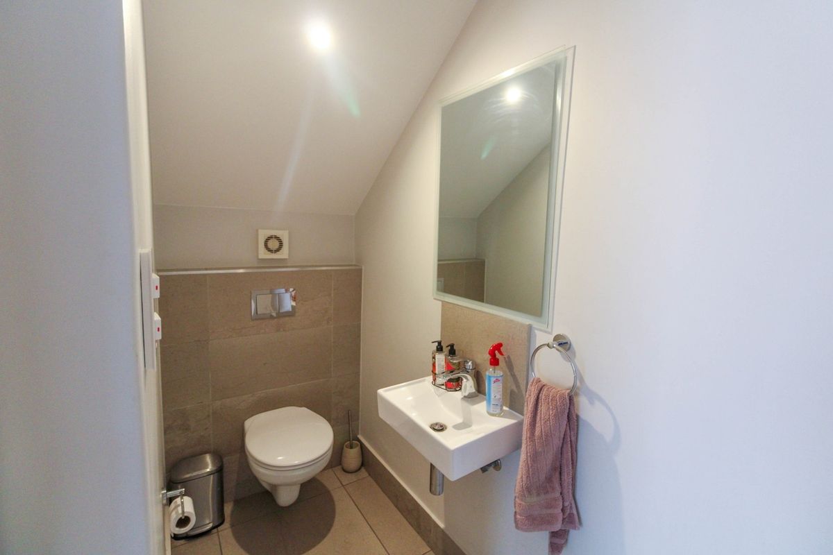 A compact guest bathroom featuring a wall-mounted toilet, modern basin, and neutral tiling under a sloped ceiling.