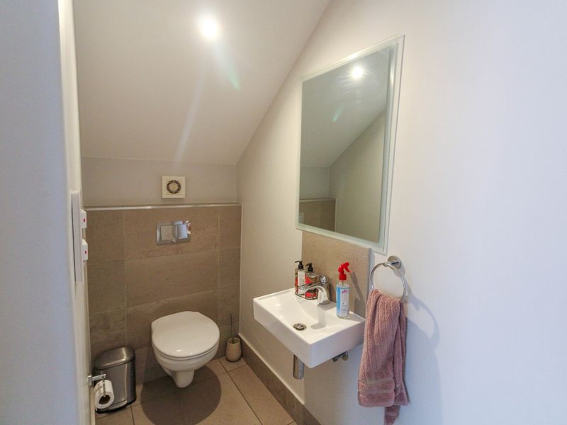 A compact guest bathroom featuring a wall-mounted toilet, modern basin, and neutral tiling under a sloped ceiling.