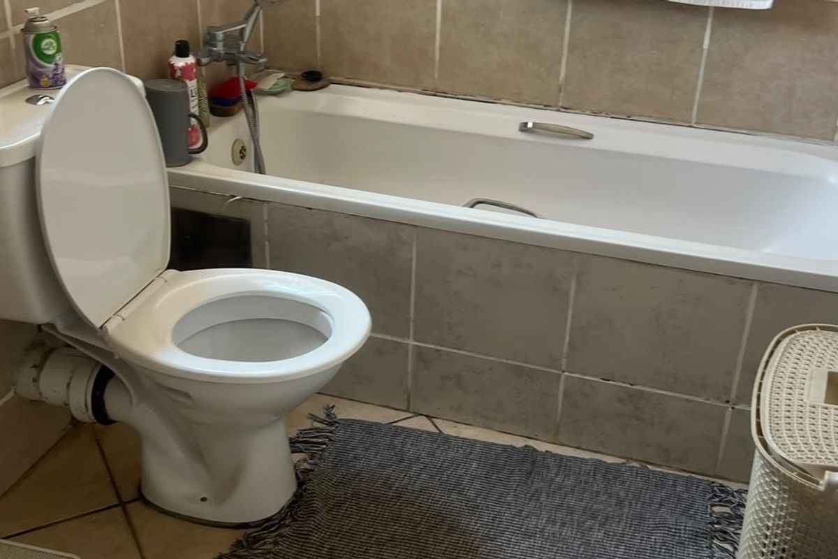 A functional bathroom featuring a standard bathtub with mixer tap and a toilet, finished with neutral wall and floor tiling.
