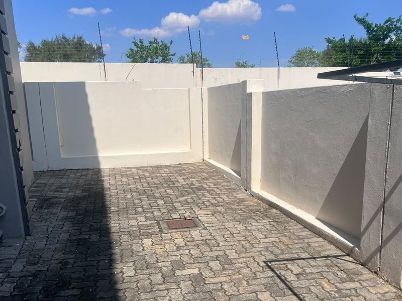 A private paved rear courtyard featuring high perimeter walls with electric fencing and a wall-mounted washing line, offering a secure outdoor utility space.